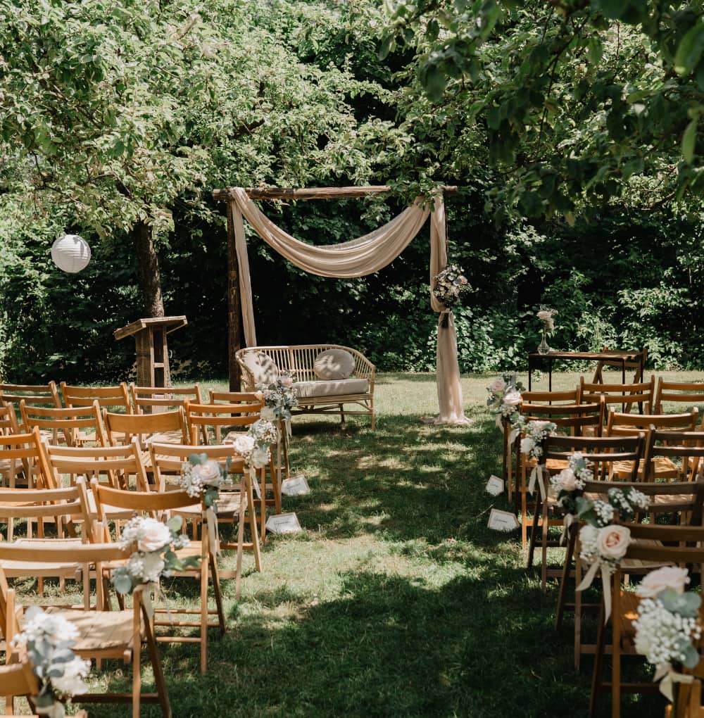 Buitenceremonie onder de bomen bij Dengh met houten stoelen en witte decoratie