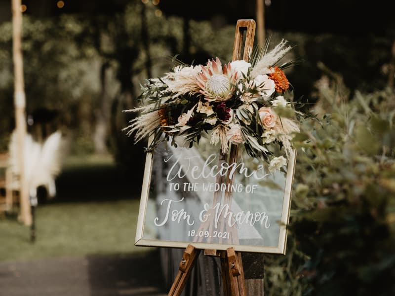 Sfeerfoto van een glazen welkomstbord op ezel met bloemstuk